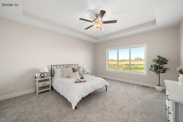 carpeted bedroom with a tray ceiling and ceiling fan