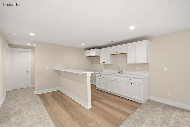 kitchen featuring a textured ceiling, light wood-type flooring, white cabinetry, and sink