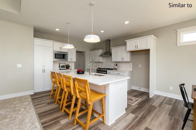 kitchen with a kitchen island with sink, sink, wall chimney exhaust hood, white cabinetry, and stainless steel appliances