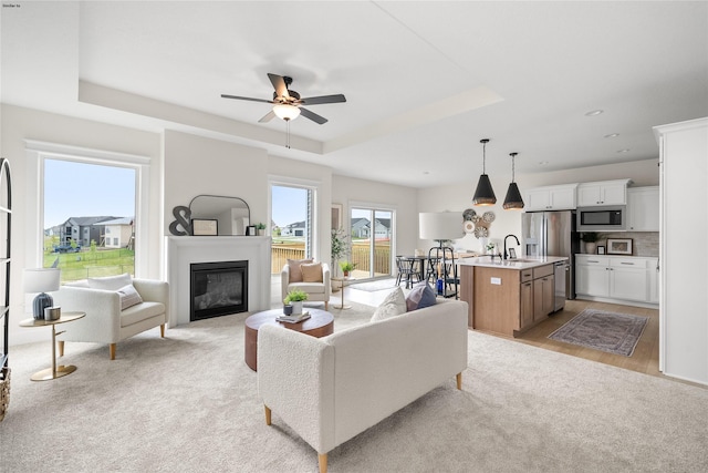 living room featuring ceiling fan, a raised ceiling, light colored carpet, and sink