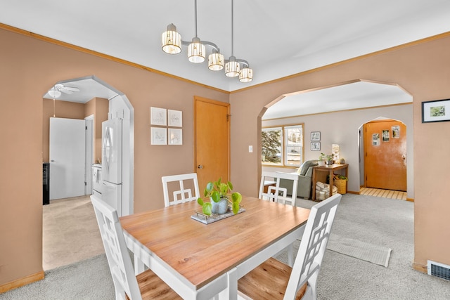 carpeted dining room with ceiling fan and crown molding