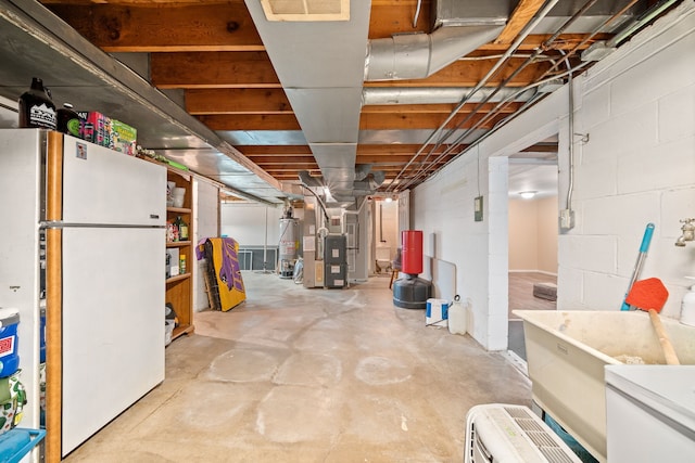 basement featuring gas water heater, white fridge, and heating unit