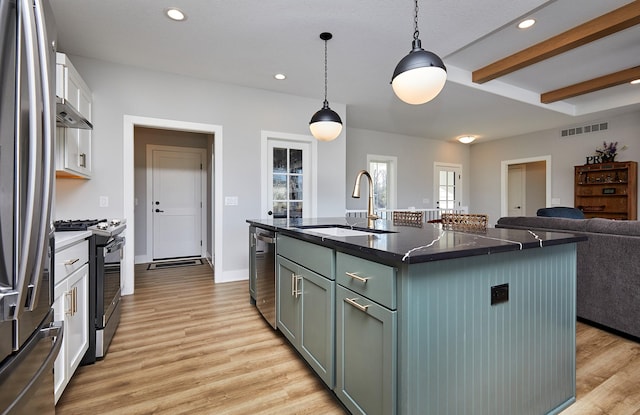 kitchen with stainless steel appliances, sink, white cabinets, hanging light fixtures, and an island with sink