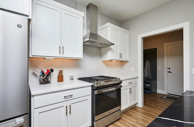 kitchen with wall chimney exhaust hood, white cabinetry, stainless steel appliances, and tasteful backsplash