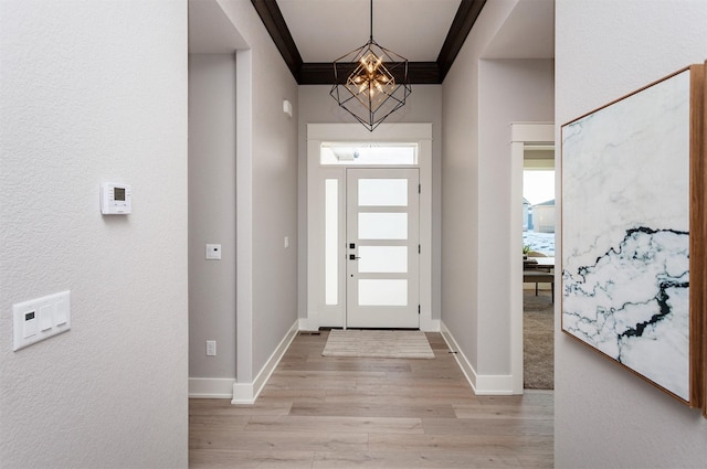 foyer entrance featuring light wood-type flooring, ornamental molding, and a chandelier