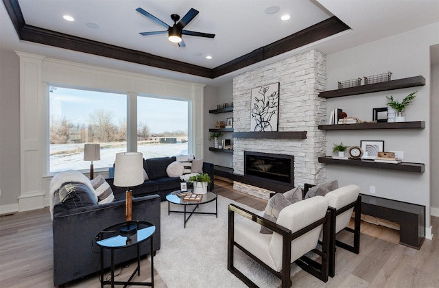 living room with a tray ceiling, a fireplace, light hardwood / wood-style flooring, and ornamental molding