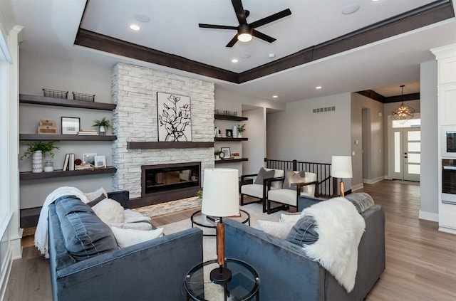 living room with ceiling fan with notable chandelier, crown molding, light wood-type flooring, and a fireplace