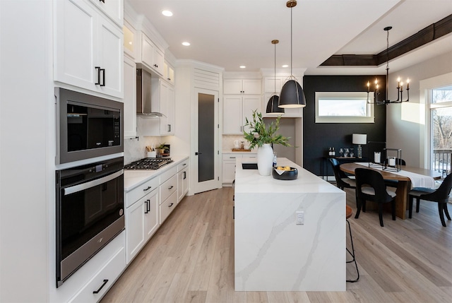 kitchen featuring pendant lighting, wall chimney range hood, white cabinetry, stainless steel appliances, and a chandelier