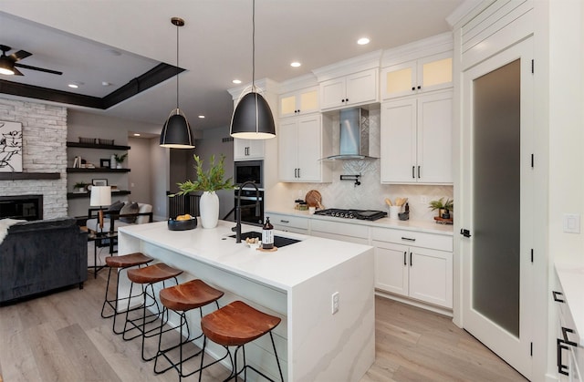 kitchen featuring tasteful backsplash, wall chimney exhaust hood, a kitchen island with sink, white cabinets, and hanging light fixtures