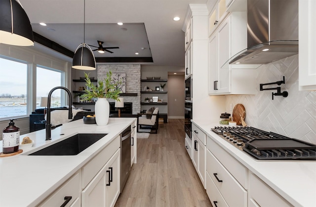 kitchen featuring sink, hanging light fixtures, wall chimney range hood, white cabinets, and appliances with stainless steel finishes