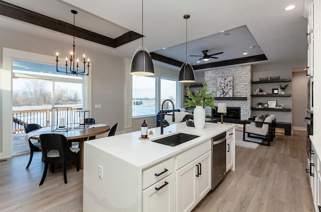 kitchen with a large fireplace, decorative light fixtures, a tray ceiling, a center island with sink, and white cabinets