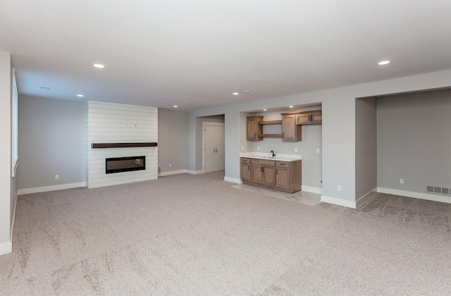 unfurnished living room featuring sink, light colored carpet, and a fireplace