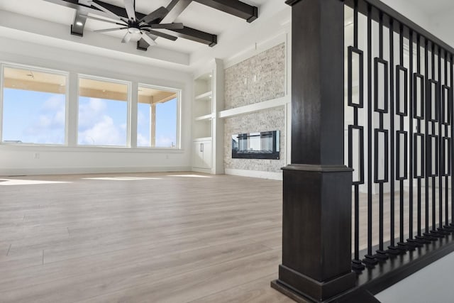 unfurnished living room featuring beamed ceiling, a fireplace, light wood-style flooring, and built in features