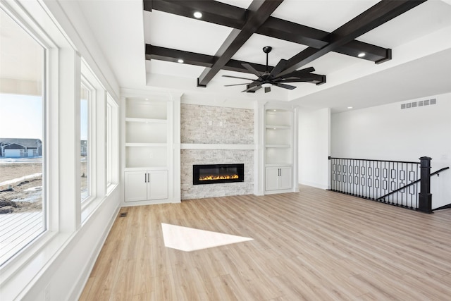 unfurnished living room featuring beam ceiling, light wood finished floors, visible vents, a stone fireplace, and coffered ceiling