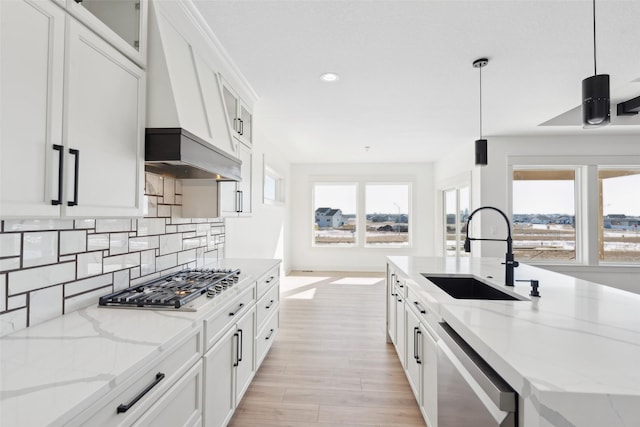 kitchen featuring light stone counters, hanging light fixtures, appliances with stainless steel finishes, white cabinets, and a sink