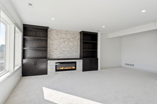 unfurnished living room with a healthy amount of sunlight, a fireplace, visible vents, and light carpet