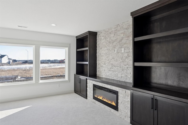 unfurnished living room featuring a large fireplace, visible vents, built in features, and light colored carpet