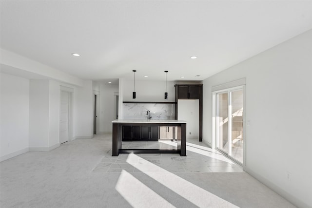 kitchen featuring recessed lighting, light countertops, hanging light fixtures, a kitchen island with sink, and baseboards