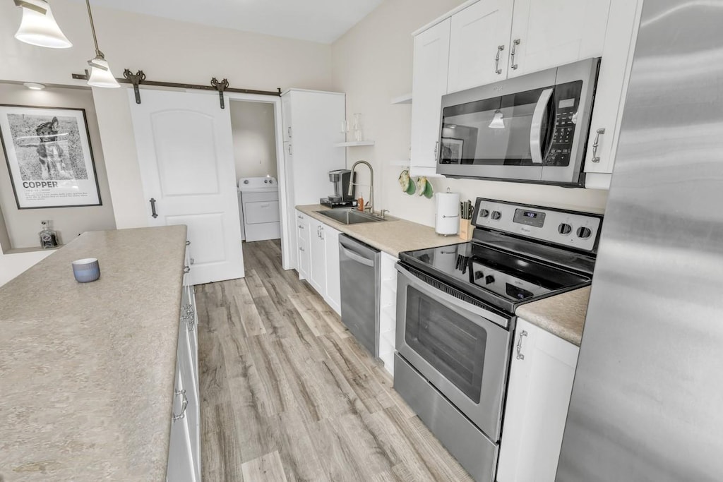 kitchen featuring white cabinetry, sink, a barn door, pendant lighting, and appliances with stainless steel finishes