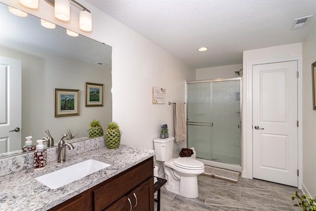 bathroom featuring vanity, toilet, a shower with shower door, and a textured ceiling