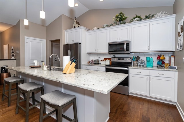 kitchen featuring appliances with stainless steel finishes, backsplash, vaulted ceiling, and an island with sink