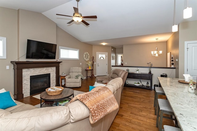 living room featuring a stone fireplace, lofted ceiling, ceiling fan with notable chandelier, and hardwood / wood-style flooring