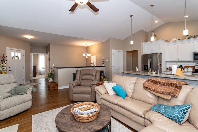 living room with ceiling fan with notable chandelier, dark hardwood / wood-style floors, vaulted ceiling, and sink