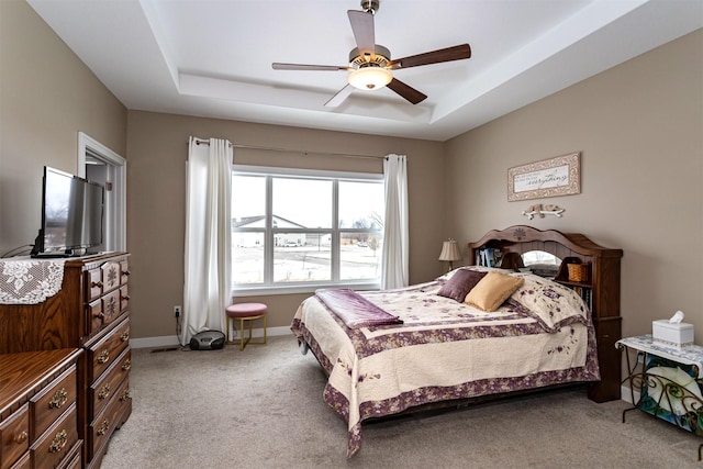 bedroom with a raised ceiling, ceiling fan, and light colored carpet