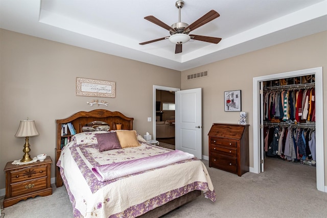 carpeted bedroom with ceiling fan, a raised ceiling, and a closet