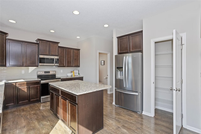 kitchen featuring stainless steel appliances, dark hardwood / wood-style flooring, decorative backsplash, a kitchen island, and dark brown cabinetry