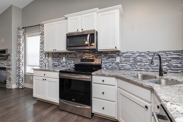 kitchen with light stone counters, stainless steel appliances, sink, white cabinets, and a stone fireplace