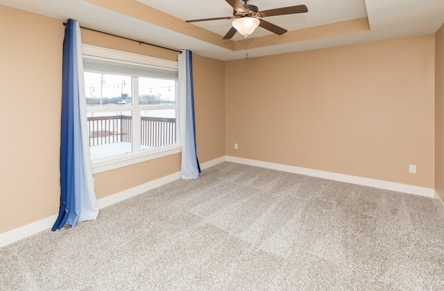 carpeted empty room with a raised ceiling and ceiling fan