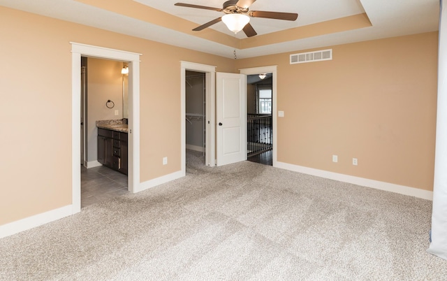 unfurnished bedroom featuring a tray ceiling, ceiling fan, a spacious closet, connected bathroom, and a closet