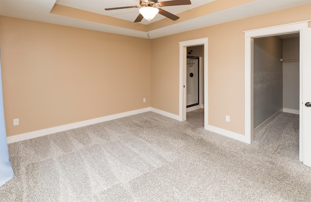 unfurnished bedroom featuring a raised ceiling, carpet flooring, ceiling fan, a spacious closet, and a closet