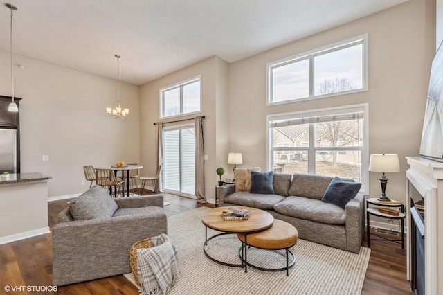 living room with a towering ceiling, an inviting chandelier, plenty of natural light, and dark wood-type flooring