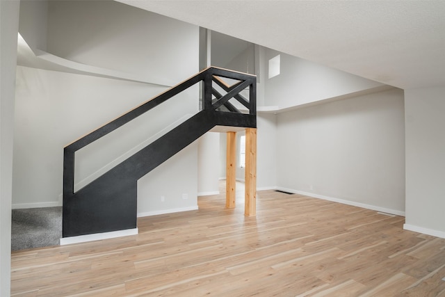 unfurnished living room with light wood-type flooring and a towering ceiling