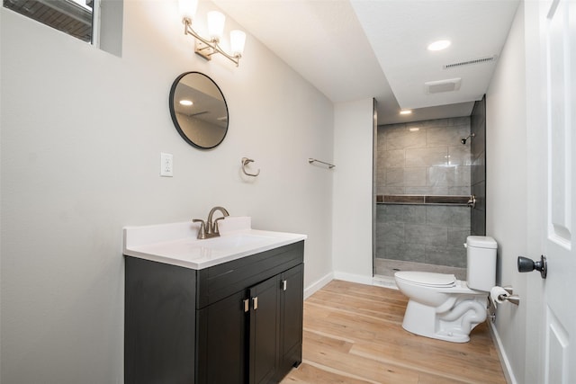 bathroom featuring wood-type flooring, vanity, a tile shower, and toilet