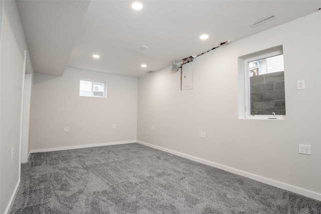 basement featuring plenty of natural light, dark carpet, and a textured ceiling