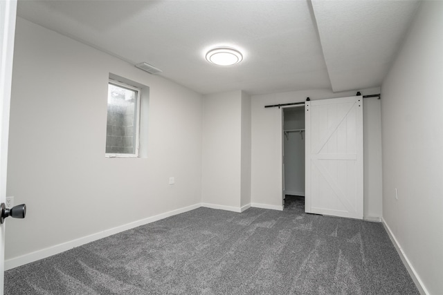 unfurnished bedroom with a barn door, a closet, dark carpet, and a textured ceiling