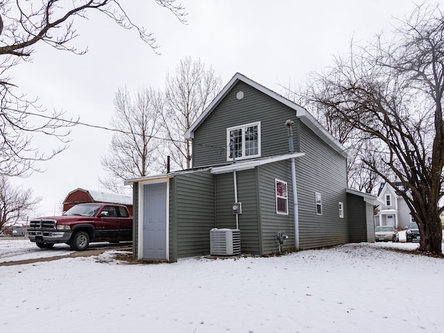 snow covered rear of property featuring central AC unit