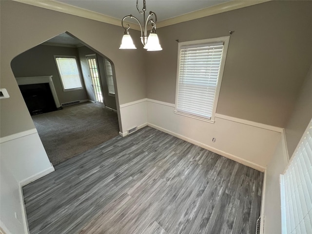 unfurnished dining area featuring baseboard heating, crown molding, dark colored carpet, and an inviting chandelier