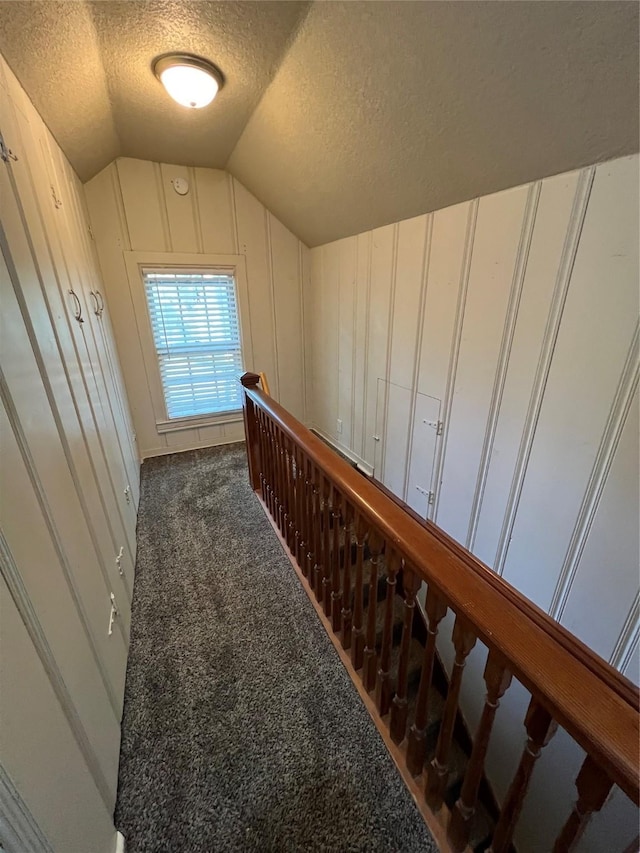 hall with a textured ceiling, dark carpet, and lofted ceiling