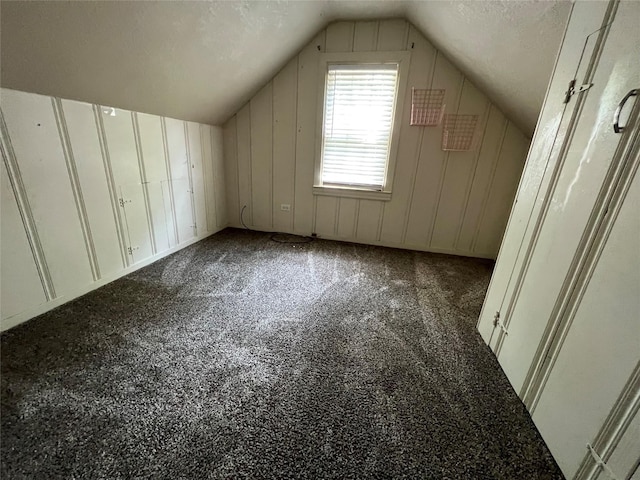 bonus room featuring dark carpet, lofted ceiling, and a textured ceiling