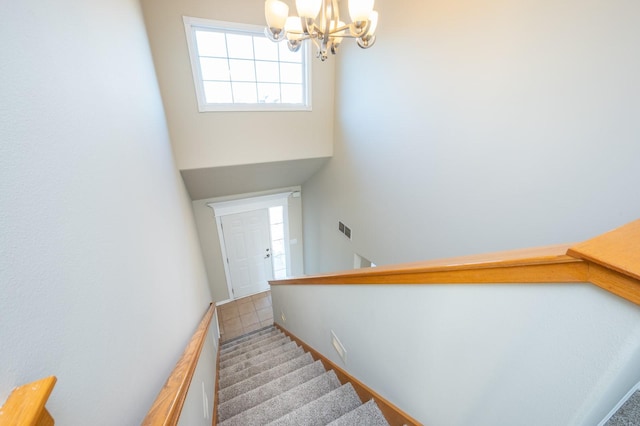 staircase with a towering ceiling, carpet floors, and an inviting chandelier