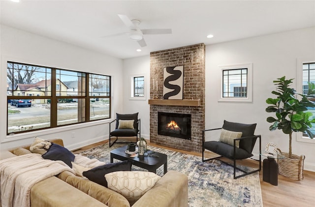 living room featuring ceiling fan, light wood-type flooring, and a brick fireplace