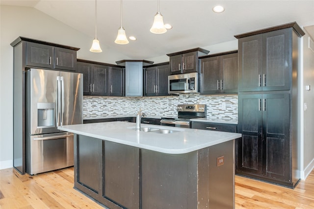 kitchen featuring appliances with stainless steel finishes, tasteful backsplash, vaulted ceiling, a kitchen island with sink, and pendant lighting