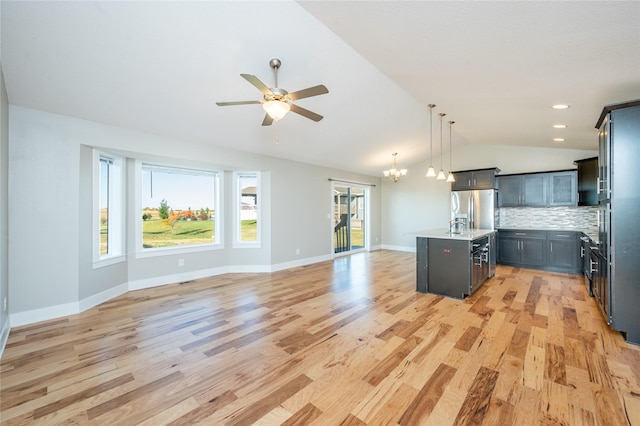 kitchen featuring stainless steel fridge, backsplash, decorative light fixtures, a center island with sink, and lofted ceiling