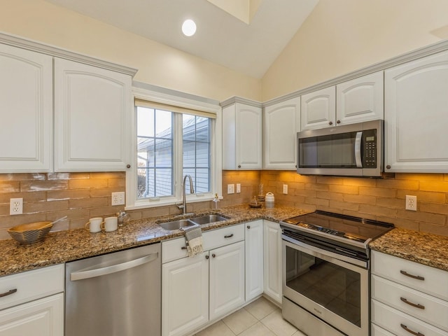 kitchen with stainless steel appliances, sink, dark stone countertops, white cabinetry, and lofted ceiling