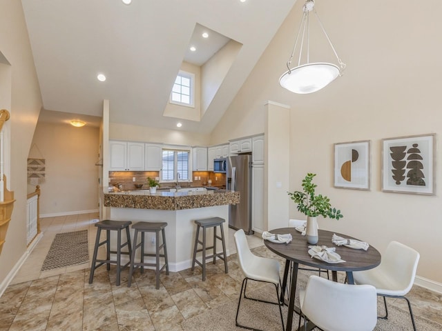 kitchen featuring a high ceiling, kitchen peninsula, appliances with stainless steel finishes, tasteful backsplash, and white cabinetry