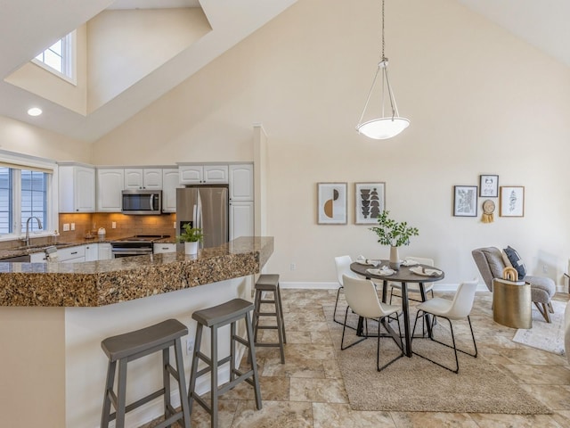 kitchen with white cabinets, tasteful backsplash, a towering ceiling, a wealth of natural light, and appliances with stainless steel finishes